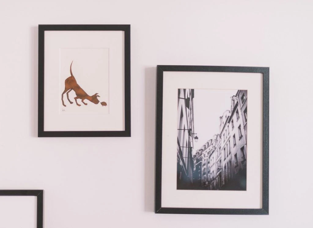 Picture frames (to the left, an illustration of a dog, and to the right a picture of buildings) mounted on a wall which be packed as a fragile item
