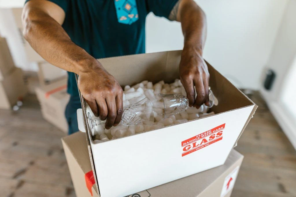 Guy packing glassware into a cardboard moving box filled with packing peanuts so he can take it to his moving storage unit