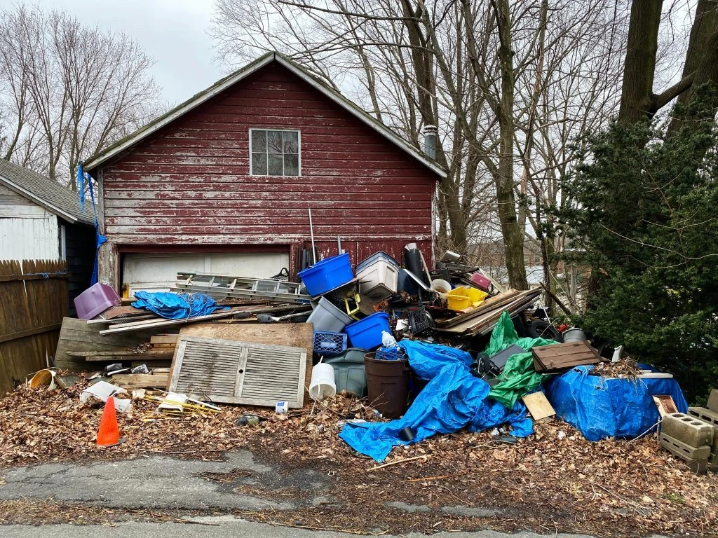 Disorganized junk piled in from of weathered garage building