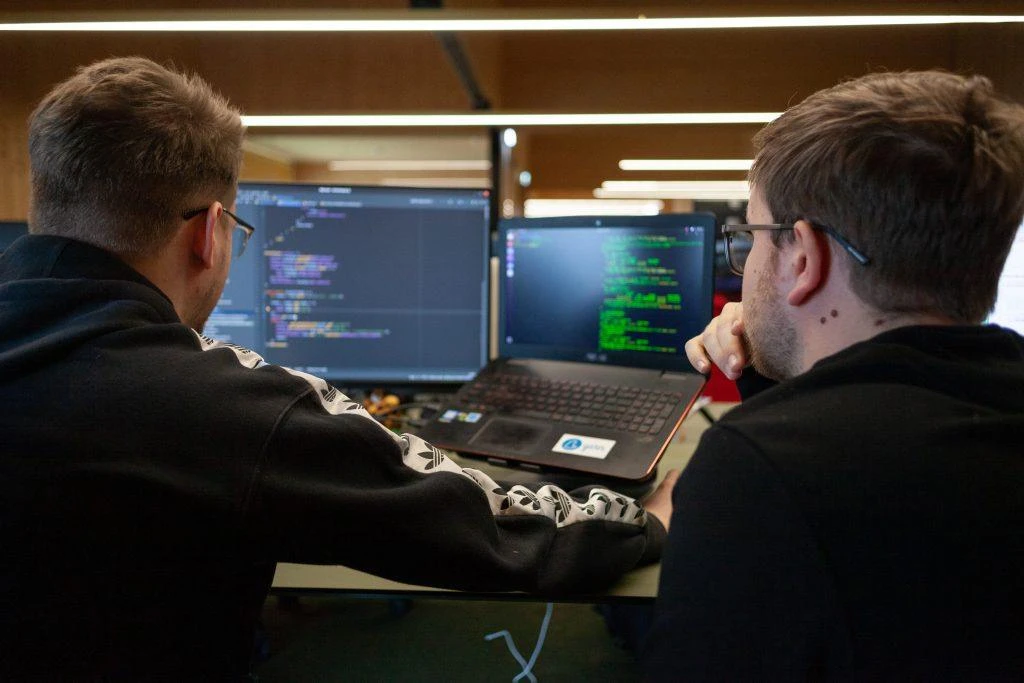 Two IT staff members working at multiple monitors reviewing code